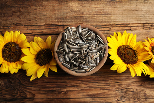Raw sunflower seeds and flowers on wooden table, flat lay