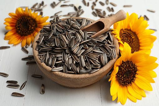 Raw sunflower seeds and flowers on white wooden table