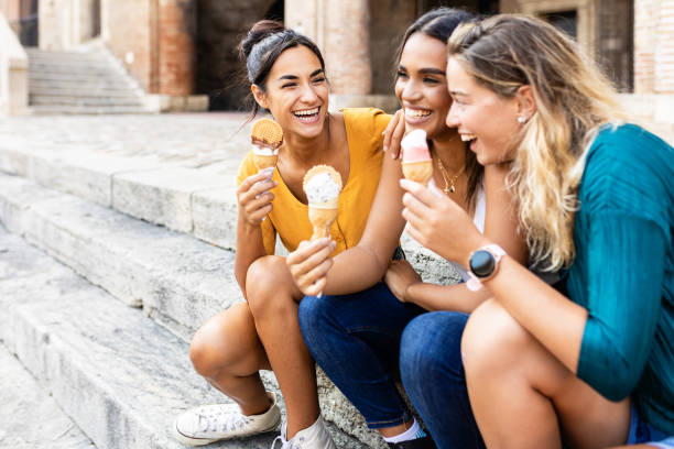 donne multirazziali felici che mangiano gelato all'aperto mentre sono sedute alle scale - asian ethnicity women young adult cheerful foto e immagini stock