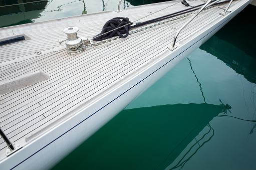 The sharp end of an elegant sailing boat with teak deck moored at marina.