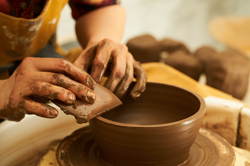 A Potter works with red clay on a Potter's wheel in the workshop.
