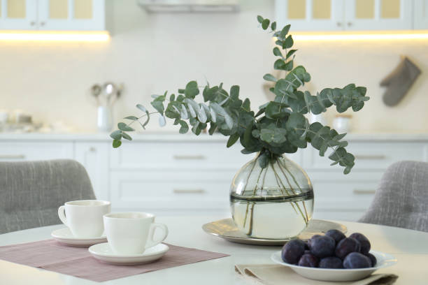 istock Beautiful eucalyptus branches,  cups of drink and fresh plums on white table in kitchen. Interior element 1388140957