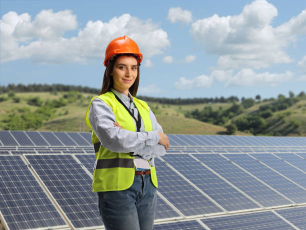 young female engineer with a safety wear standing on a solar plant - solar power station solar panel energy electrician imagens e fotografias de stock