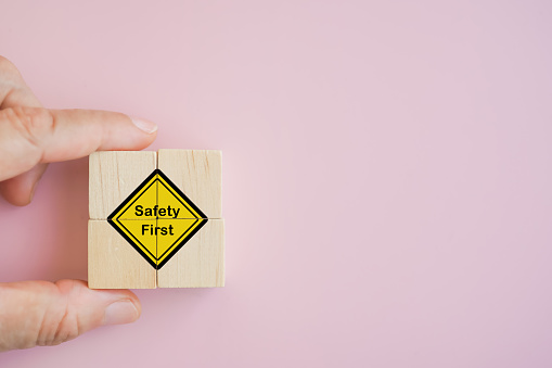 hand holds Safety first  symbols icon on wooden cubes with pink background with copy space, work safety, caution work hazards, danger surveillance, zero accident concept. Safety banner