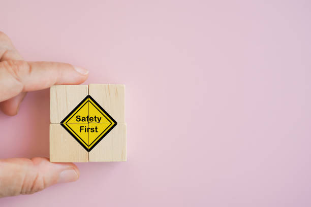 hand holds Safety first  symbols icon on wooden cubes with pink background with copy space, work safety, caution work hazards, danger surveillance, zero accident concept. Safety banner stock photo