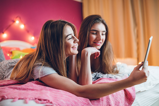 Two beautiful teenage girls having a pajamas party. Spending time on internet.