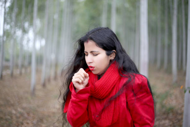 Woman wearing a bright red scarf basks in the warm sunlight while sitting outdoors in a park filled with autumn leaves. The golden light and nature create a vibrant and peaceful atmosphere, perfect for relaxation and reflection.
