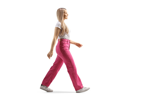 Full length profile shot of a young woman in pink jeans walking isolated on white background