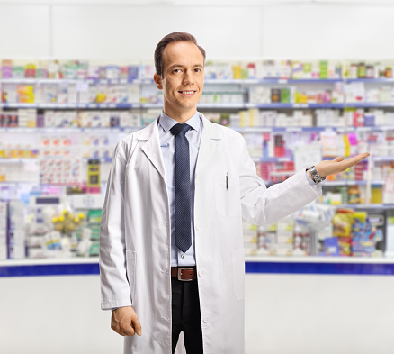 Male pharmacist showing with hand inside a pharmacy