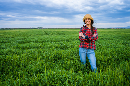 Satisfied female farmer is standing in her barley field.