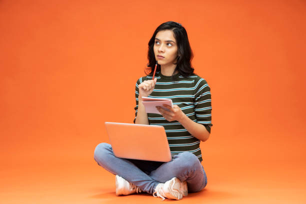 Young woman sitting on floor with laptop on orange background, stock photo stock photo
