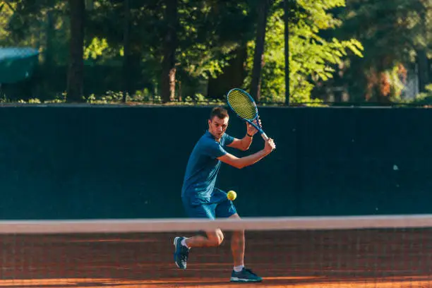 Photo of Professional equipped male tennis player beating hard the tennis ball with a backhand