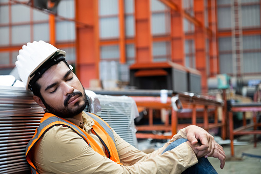 Engineer of industrial working taking a nap or fall asleep inside of factory industrial area because of long working shift. Exhausted working who need to take a rest while working