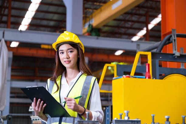 istock Selective focus at young women inspector wearing safety equipment. While doing audit for quality and safety control inside of factory area. With blurred background of heavy machine. 1388156602