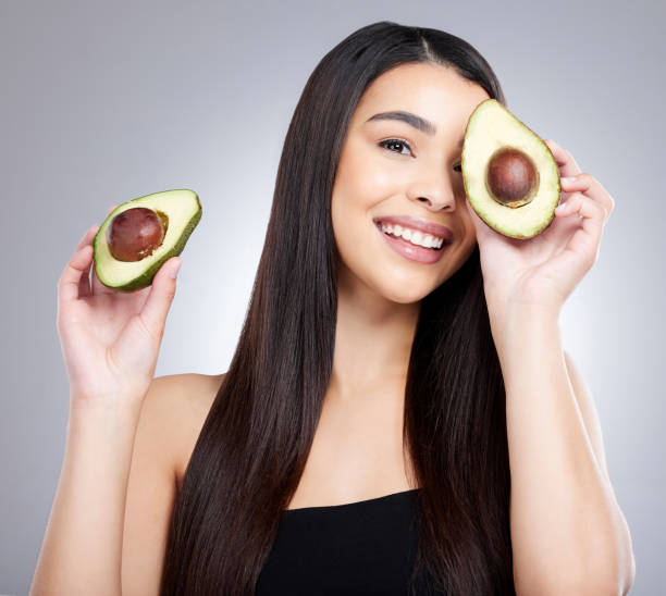 ritratto in studio di una giovane donna attraente in posa con un avocado su uno sfondo grigio - superfood avocado fruit vegetable foto e immagini stock