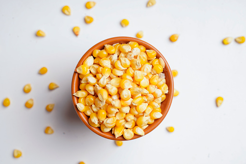 dried corn seeds in wooden bowl on white background.