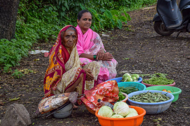 Stock photo of 40 to 70 age group two Indian women wearing saree and sitting by the roadside, selling farm fresh green vegetables in the monsoon season in India. stock photo