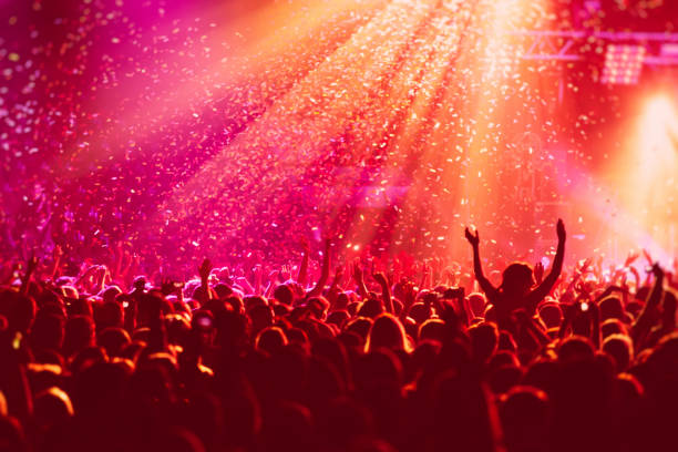 una sala de conciertos abarrotada con escenario de escena en luces rojas, espectáculo de rock, con silueta de gente, explosión de confeti colorido disparada en el aire de la pista de baile durante un festival de conciertos - concierto fotografías e imágenes de stock