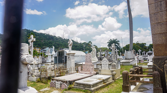 Panama City, Panama-April 2018: Small local Catholic graveyard in the city with white stone and ceramic pedestal cross and statues and colourful flowers covering the graves of dead people. Holy place.