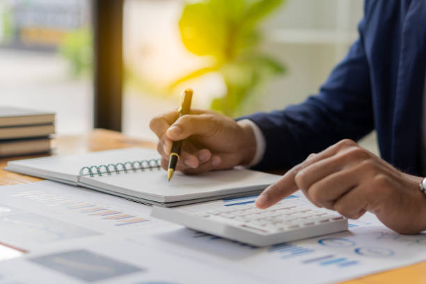 istock Hand pressing a calculator, analyzing financial documents while holding a pen in your finger. Young Asian businessman charging taxes, bills, credit card for payment, financial concept. 1388167104