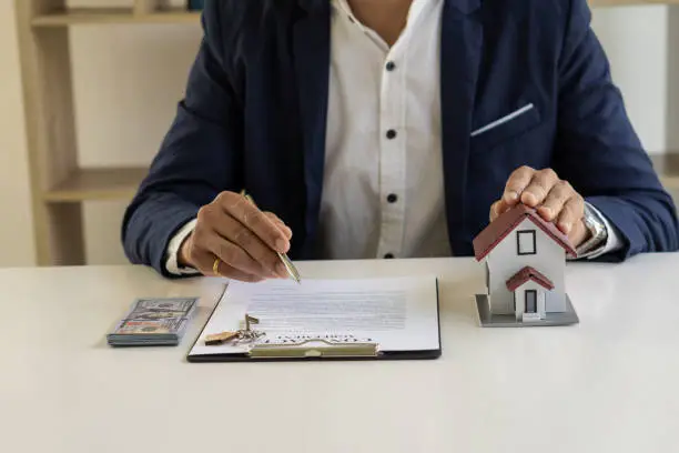 Photo of Real estate office home sales agents work with contract documents with house designs and calculators on the table.