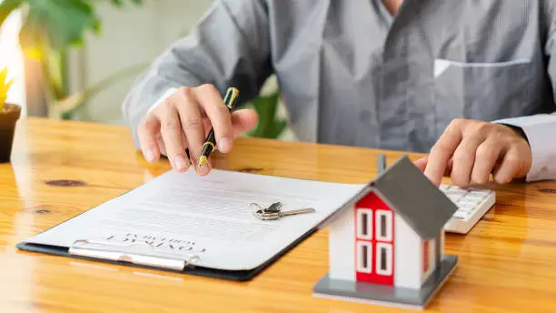 Photo of Real estate office home sales agents work with contract documents with house designs and calculators on the table.