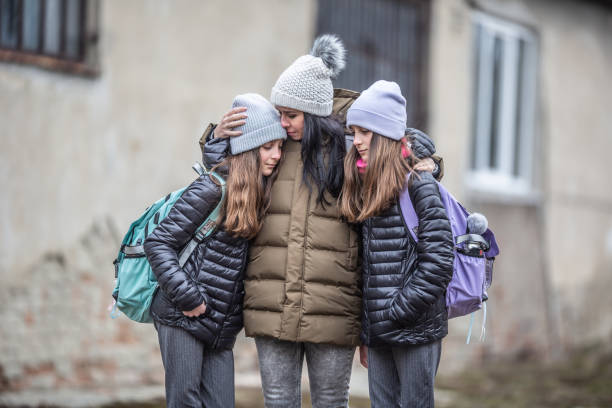 Woman kisses her daughter on forehead outdoors as they both stay in the war zone Woman kisses her daughter on forehead outdoors as they both stay in the war zone family mother poverty sadness stock pictures, royalty-free photos & images