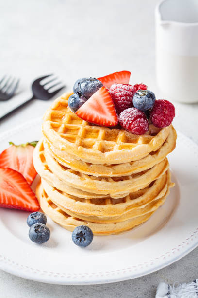 istock Homemade waffles with berries, powdered sugar and maple syrup on white plate, gray background. 1388171263