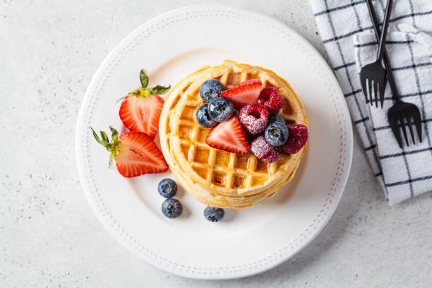 istock Homemade waffles with berries, powdered sugar and maple syrup on white plate, gray background. 1388171314