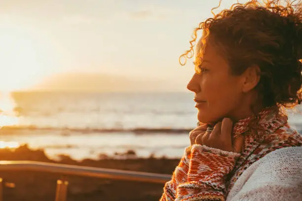 Photo of Enjoyed and serene lady dreaming and thinking outdoor with ocean beach and sunset light in background. Concept of happy lifestyle female people in outdoor leisure. Love and peace concept day