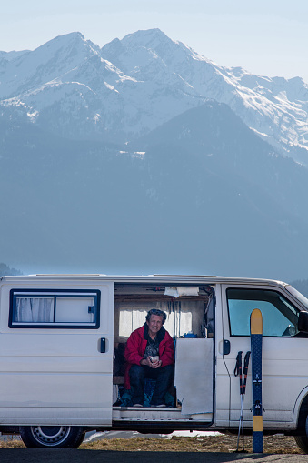 In front of a snowy mountain a man sitting in his converted mini van