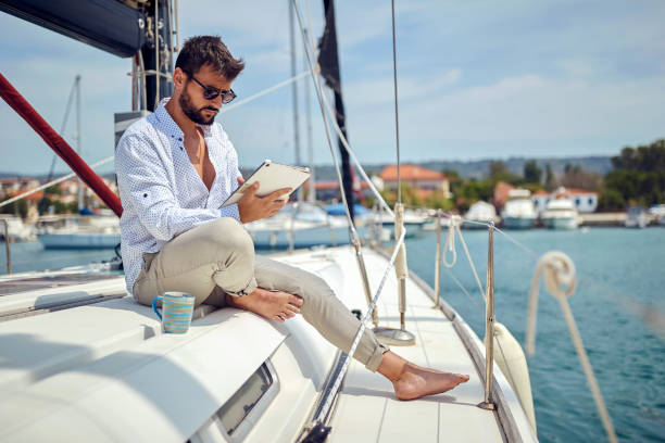 istock A young man watching a tablet content while sitting on a yacht and riding through the dock on the seaside. Summer, sea, vacation 1388174270