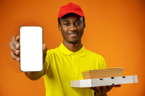 istock African courier guy showing smartphone with blank screen and holding box in studio 1388174362
