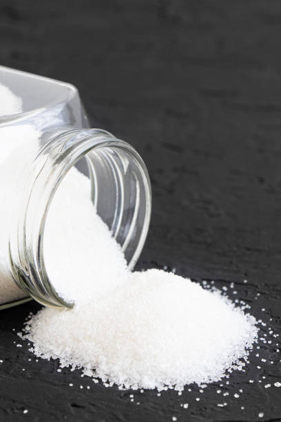 istock Glass jar with sugar black background.Diabetes. Scattered white sugar on a black table. Copy space. Place for text.Extra calories. Vertical orientation 1388174773