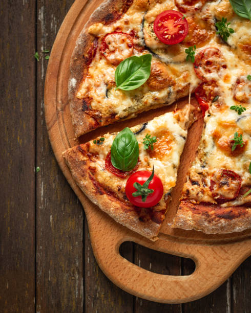 istock Vegetarian pizza with addition eggplants, cherry tomatoes and aromatic basil herbs, divided into portions on a wooden background, top view 1388177797