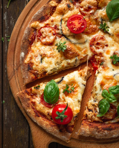 istock Vegetarian pizza with addition eggplants, cherry tomatoes and aromatic basil herbs, divided into portions on a wooden background, top view 1388177798