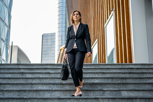 beautiful mature adult business woman in a suit walking in the finance district, confident and professional female lawyer going to the court of justice