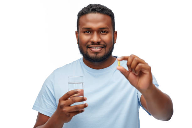 homem afro-americano com pílula e copo de água - fish oil healthy eating capsule isolated - fotografias e filmes do acervo