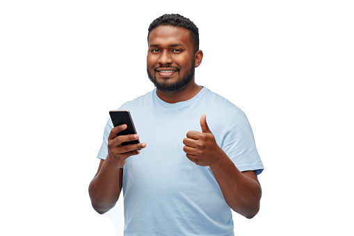 technology and people concept - happy young african american man with smartphone showing thumbs up over white background