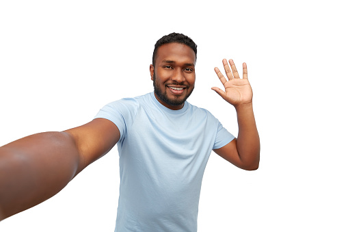 people, grooming and beauty concept - portrait of happy smiling young african american man taking selfie and waving hand over white background