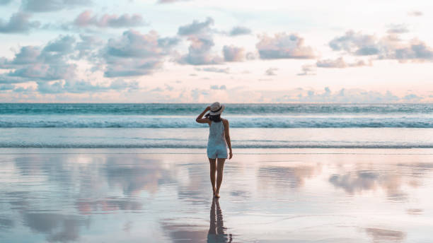 rückansicht der jungen erwachsenen touristischen asiatischen frau zu fuß entspannen auf strand sand mit schönen dramatischen sonnenuntergang himmel - activity asia atmosphere beach stock-fotos und bilder