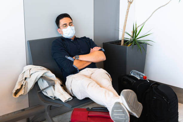 Man with protective face mask sleeps in chair in waiting room at the airport surrounded by many luggage. Travel during pandemic, and delays flights concept. Man with protective face mask sleeps in chair in waiting room at the airport surrounded by many luggage. Travel during pandemic, and delays flights concept. voyager 1 stock pictures, royalty-free photos & images