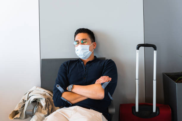 Front view young man with protective face mask sleeps sitting on a chair in a waiting room in airport during pandemic. Front view young man with protective face mask sleeps sitting on a chair in a waiting room in airport during pandemic. voyager 1 stock pictures, royalty-free photos & images
