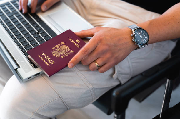 istock Close-up male hand holding Spanish European passport while using computer laptop. Travel concept. 1388191449
