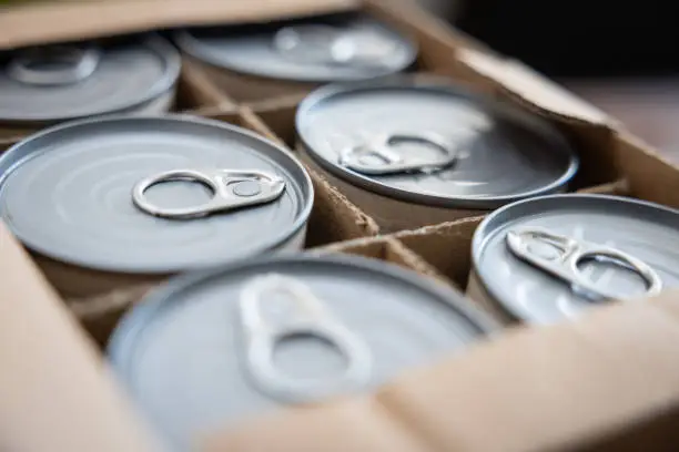Food cans in an open cardboard box. Concept image for supply chain disruption, food shortage, stockpiling in times of war. Selective focus.