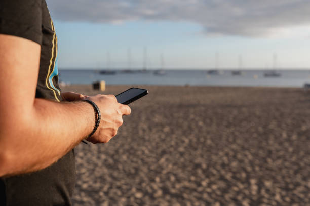 istock Unrecognizable young man using smartphone at the sea during sunset. 1388192015