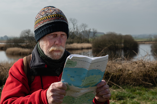 Senior man checking his map while standing beside a river in a remote rural location in Scotland