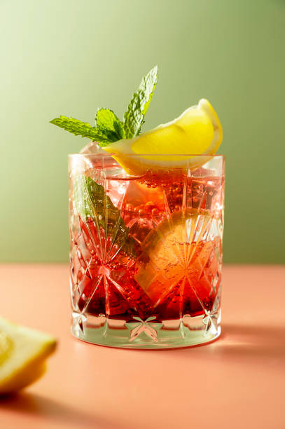 eisiger früchtetee oder kalter beerendrink im glas mit frischen minzblättern. erfrischendes sommergetränk. bunter rosa und grüner hintergrund. - mint tea lemon tea leaves glass stock-fotos und bilder