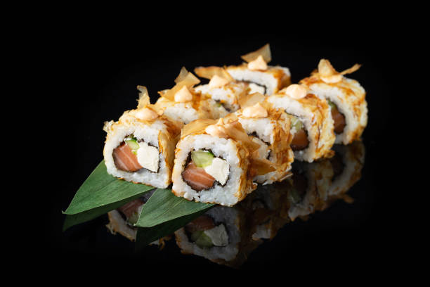 istock Traditional delicious fresh sushi roll set on a black background with reflection. Sushi roll with rice, nori, cream cheese, tobiko caviar, avocado. Sushi menu. Japanese kitchen. Asian food 1388194019