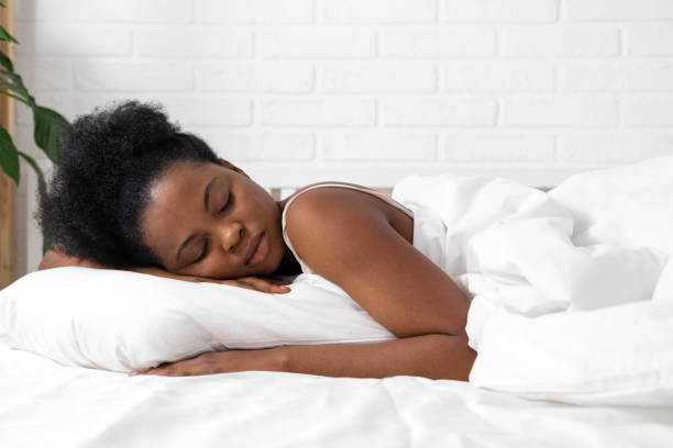 istock African American woman with hands under cheek sleeping in bed with white bedding 1388199856